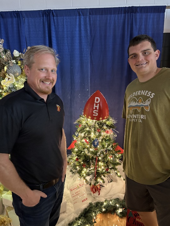 Two men standing next to a christmas treeDescription automatically generated